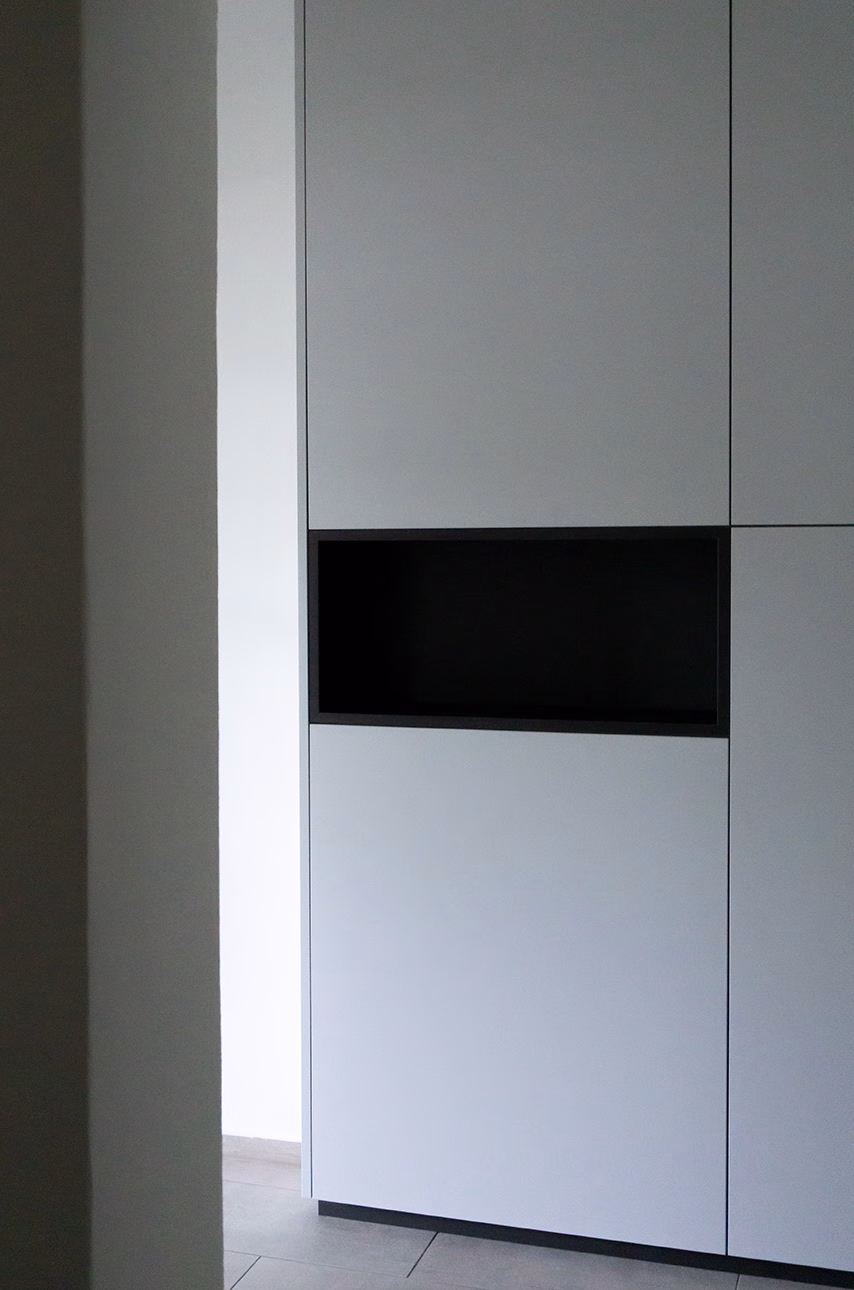 Ein eleganter, raumhoher Einbauschrank aus dem Projekt "K112" der Firma Wolter Furniture. Die schlichten, weißen Fronten werden durch ein offenes, schwarz gerahmtes Fach akzentuiert, das für zusätzlichen Stauraum oder Dekoration genutzt werden kann.